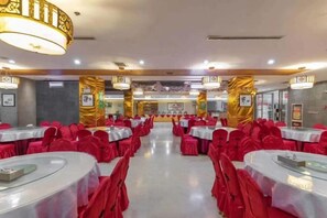 Un salón de banquetes con mesas redondas y sillas, un pasillo central y columnas decorativas.