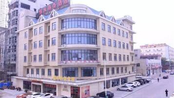 A multi-story hotel with a curved facade, multiple balconies, and a parking lot with several cars.