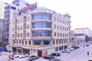 A multi-story hotel with a curved facade, multiple balconies, and a parking lot with several cars. - Sheng He Business Hotel (Tongchuan)