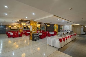 Une salle de banquet avec de nombreuses tables rondes, des chaises rouges et une scène.