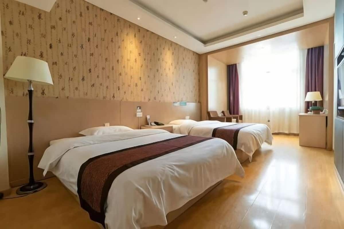 Une chambre d’hôtel avec deux lits, une table de chevet avec une lampe, une commode et une grande fenêtre avec des rideaux.