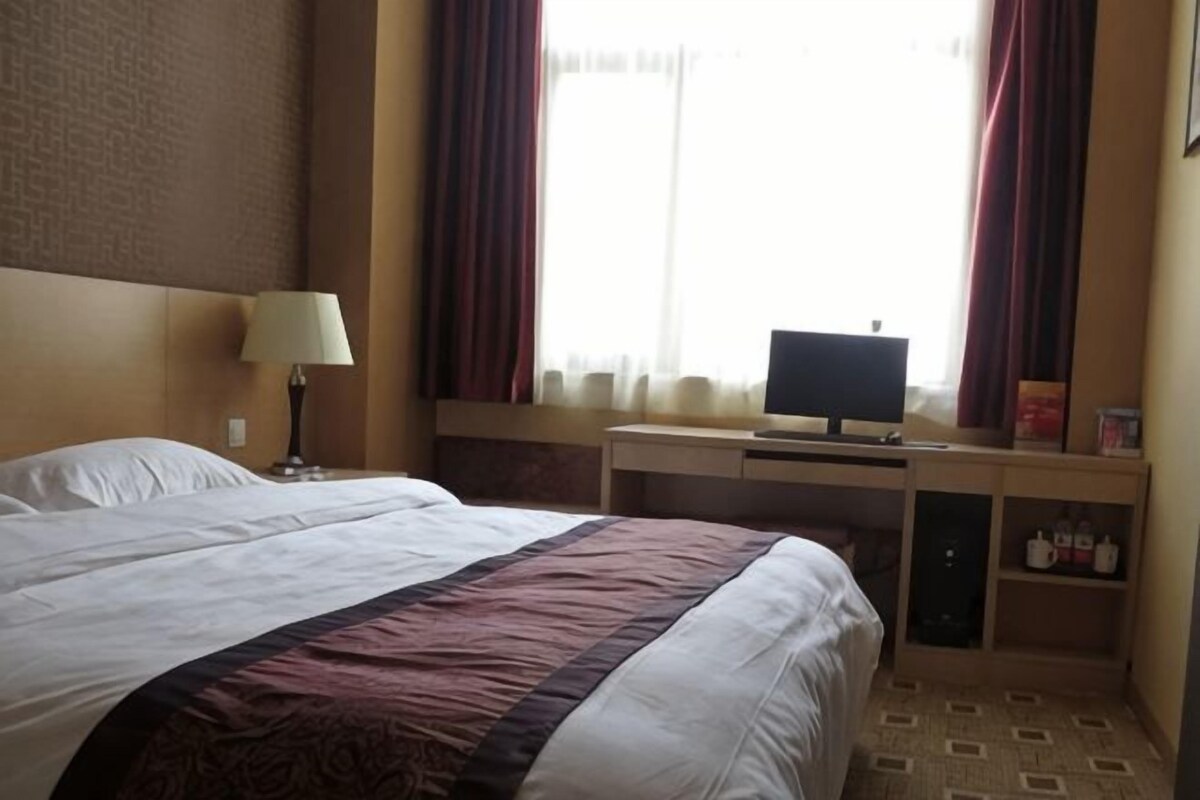 Une chambre d’hôtel avec un lit, un bureau équipé d’un ordinateur et une fenêtre avec des rideaux.