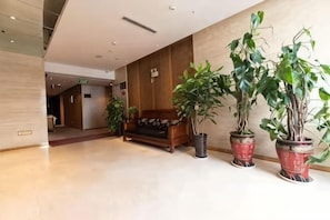 A lobby with a reception desk, potted plants, and a wooden bench. - Sheng He Business Hotel (Tongchuan)