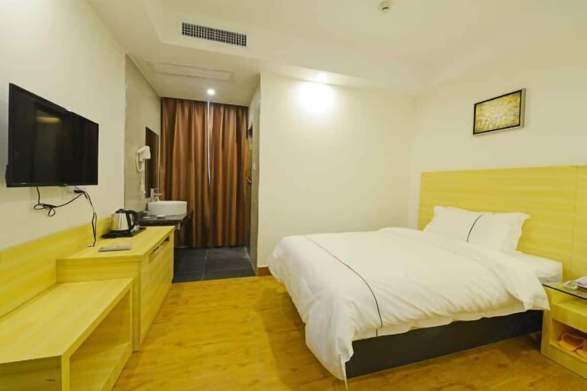 A hotel room with a bed, a desk, a television, and a bathroom visible through a curtain.