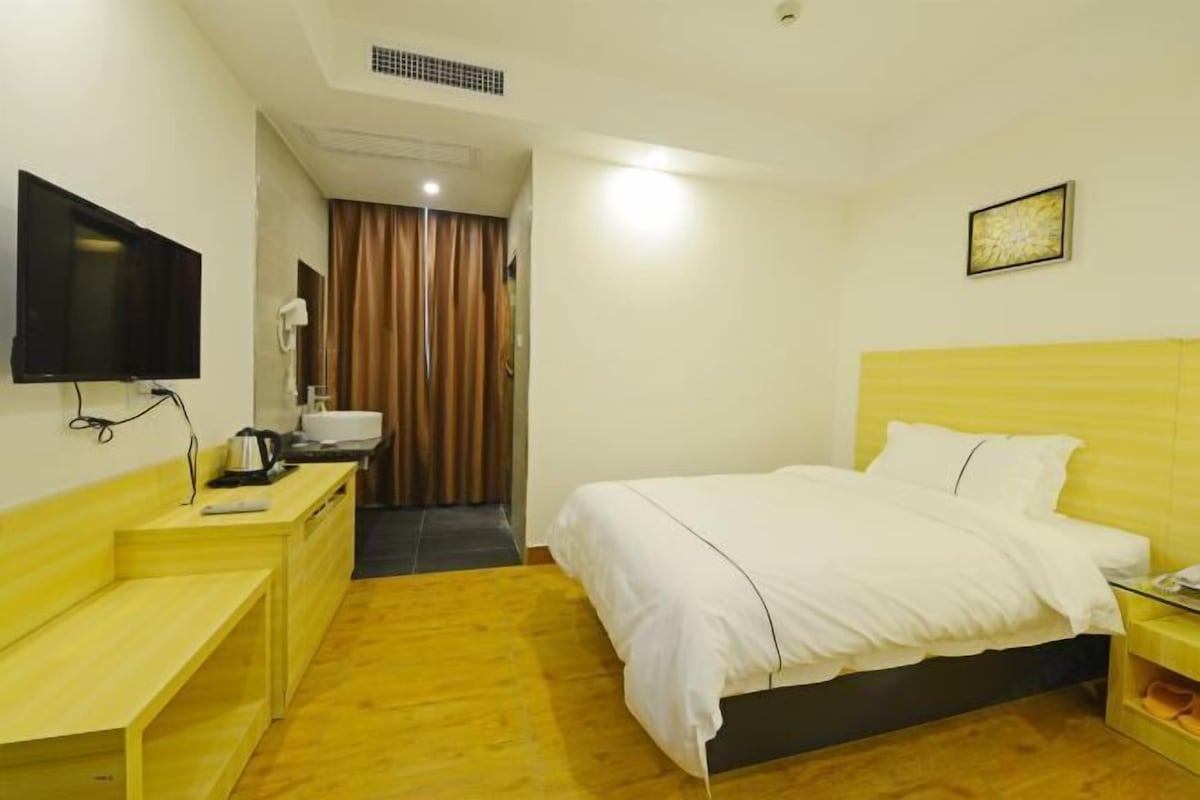 Una habitación de hotel con una cama, un escritorio con televisor, un espejo y una ventana con cortinas.