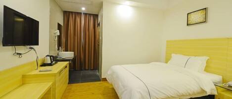 A hotel room with a bed, a desk with a television, a mirror, and a window with curtains.