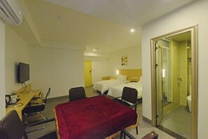 Habitación de hotel con cama, escritorio con silla, televisión y baño visible a través de una puerta abierta.