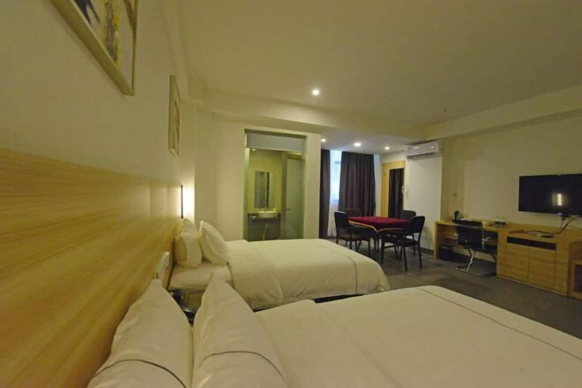 A hotel room with two beds, a desk, a chair, a television, and a bathroom visible through an open door.