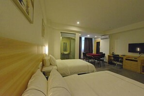 Habitación de hotel con dos camas, un escritorio, una silla, un televisor y baño visible a través de una puerta abierta.