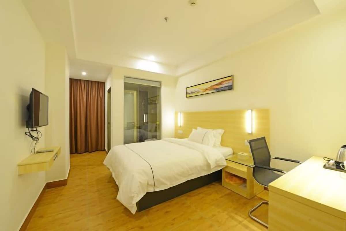 A hotel room with a bed, a desk, a chair, a television, and a painting on the wall.