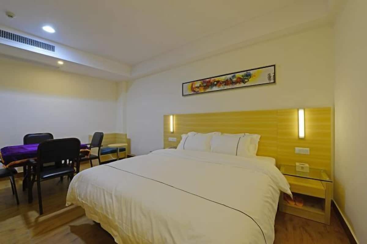 A hotel room with a large bed, a desk with chairs, a small table, and a painting on the wall.