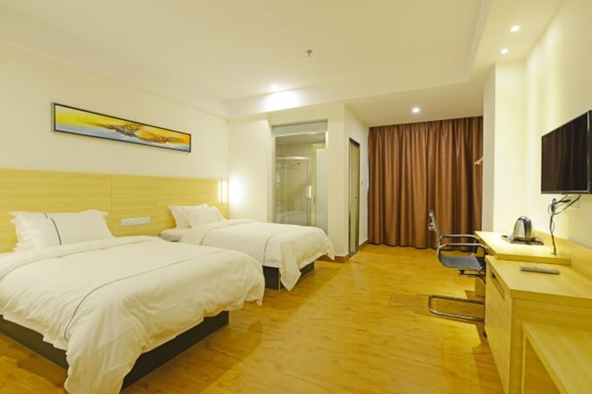 Habitación de hotel con dos camas, un escritorio con silla, televisión y un cuadro en la pared.