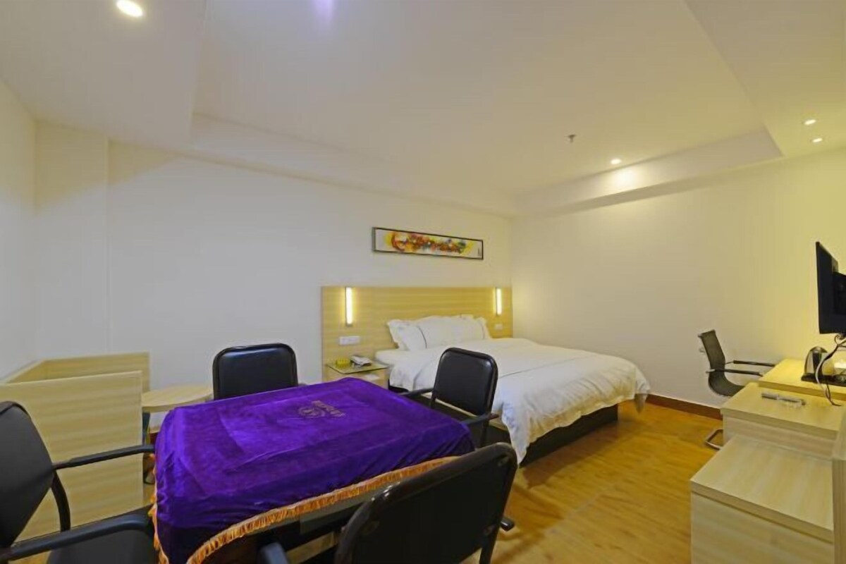 Una habitación de hotel con cama, escritorio, silla, una mesita y mantel morado.