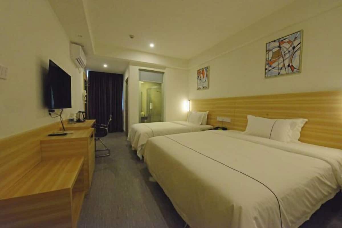 A hotel room with two beds, a desk, a TV, and artwork on the walls.