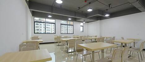 Un salón de conferencias con varias mesas y sillas, ventanas amplias y un techo alto con tuberías a la vista.