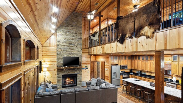 A spacious living area with a stone fireplace, a large leather sofa, and a high ceiling with exposed wooden beams.
