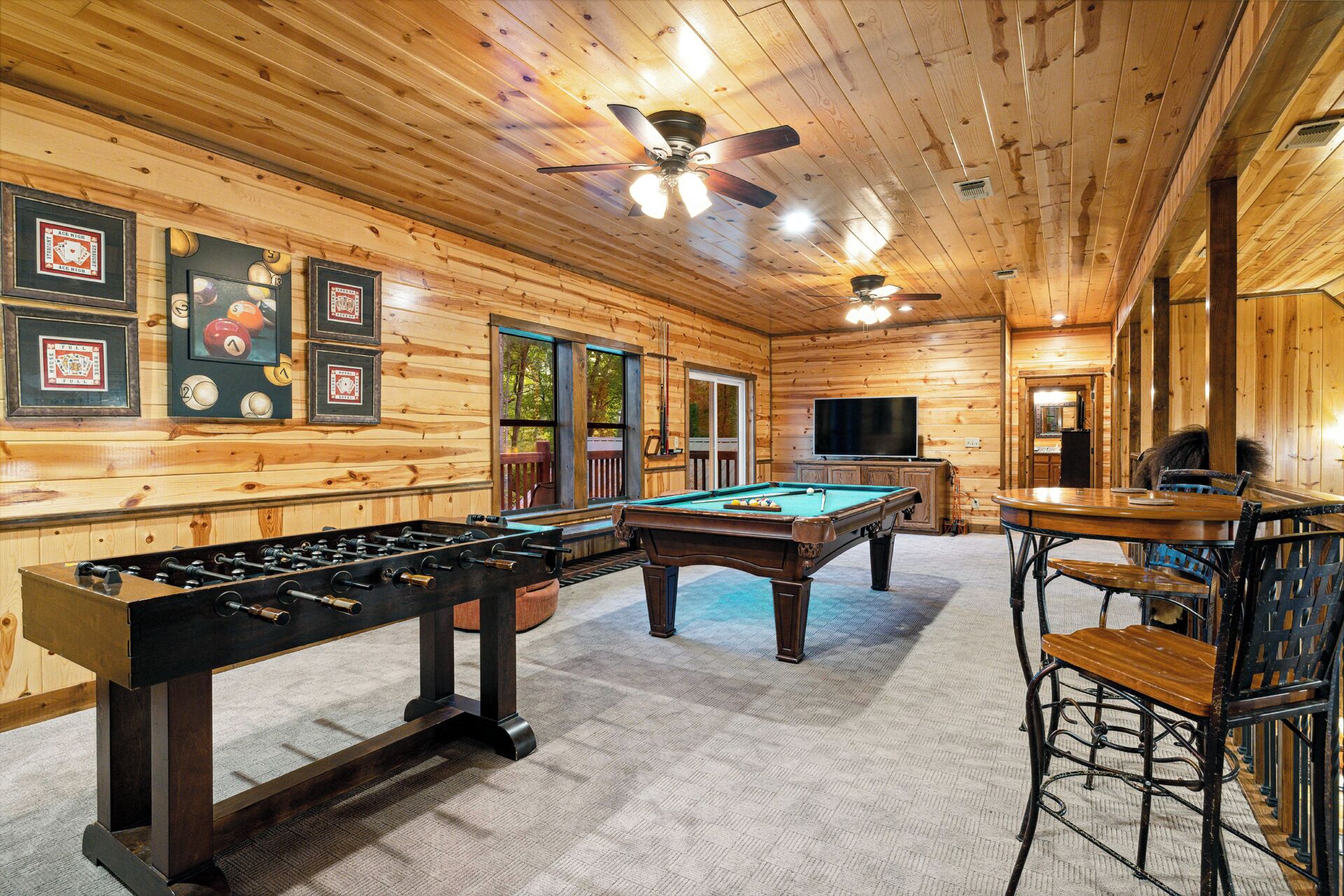 Ein Zimmer mit Holzboden, das ein Kicker, ein Billardtisch und eine Bar mit Hockern bietet.