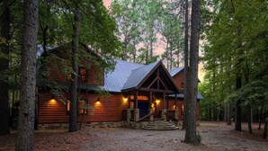 A log cabin with a stone foundation, surrounded by tall trees.