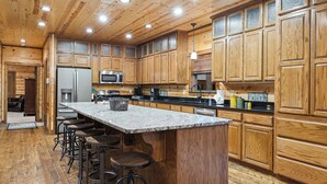 A spacious kitchen with wooden cabinets, a granite countertop, and a central island with stools.