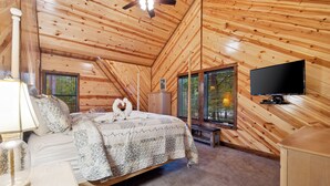 A cozy, sloped-roof bedroom with a bed, a television, and a window with blinds.