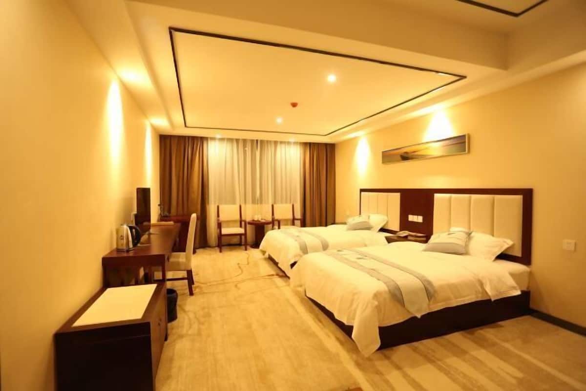 A hotel room with two beds, a desk, and a chair.