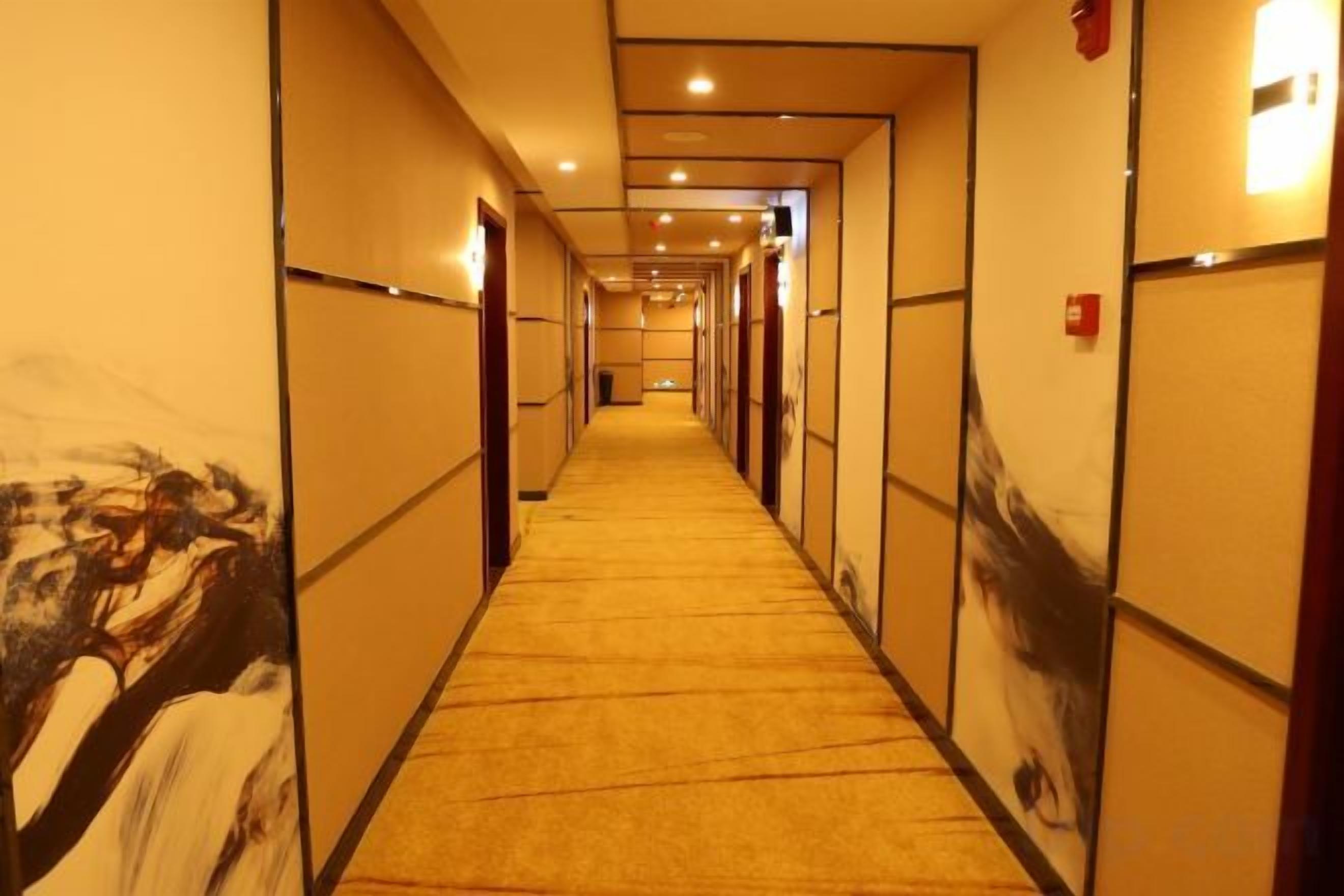 A hotel corridor with doors on both sides, carpeted flooring, and recessed lighting.