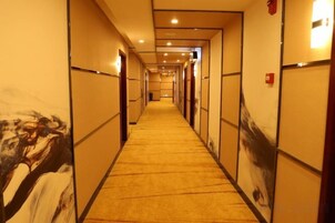 A hotel corridor with doors on both sides, carpeted flooring, and recessed lighting.