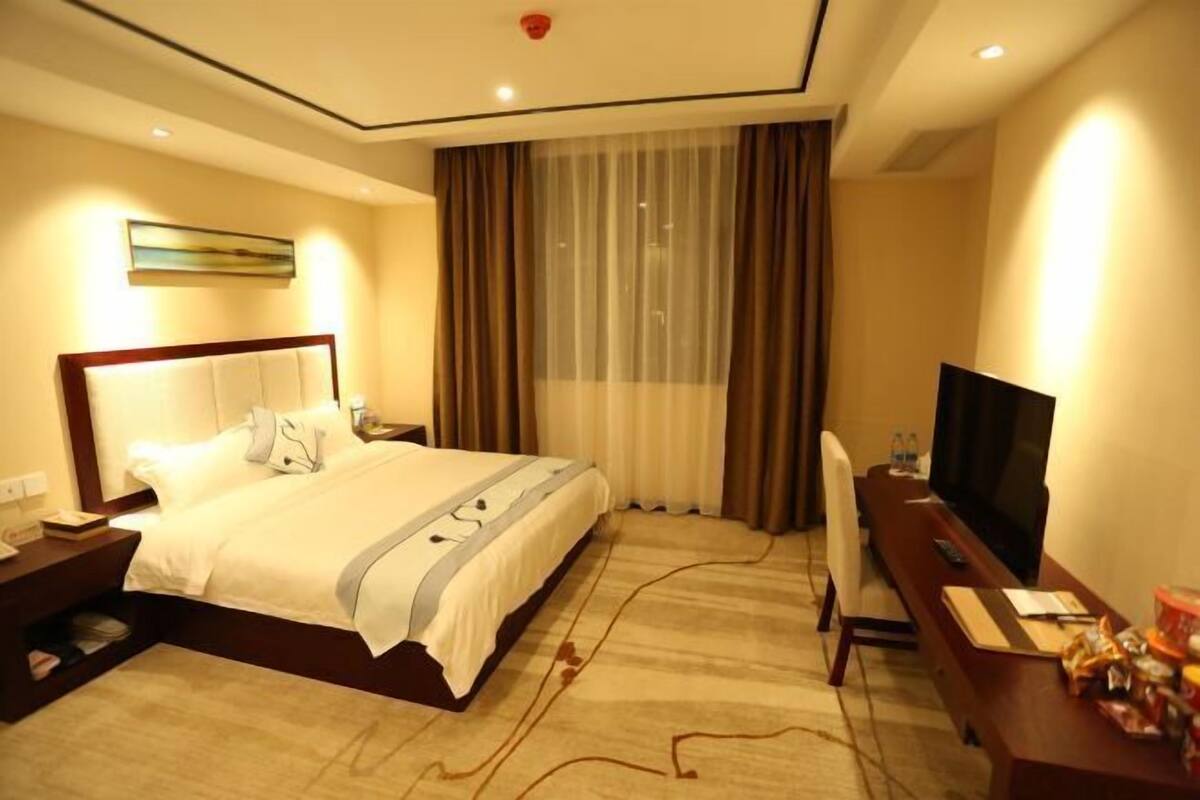 A hotel room with a large bed, a desk with a TV, and a window with curtains.