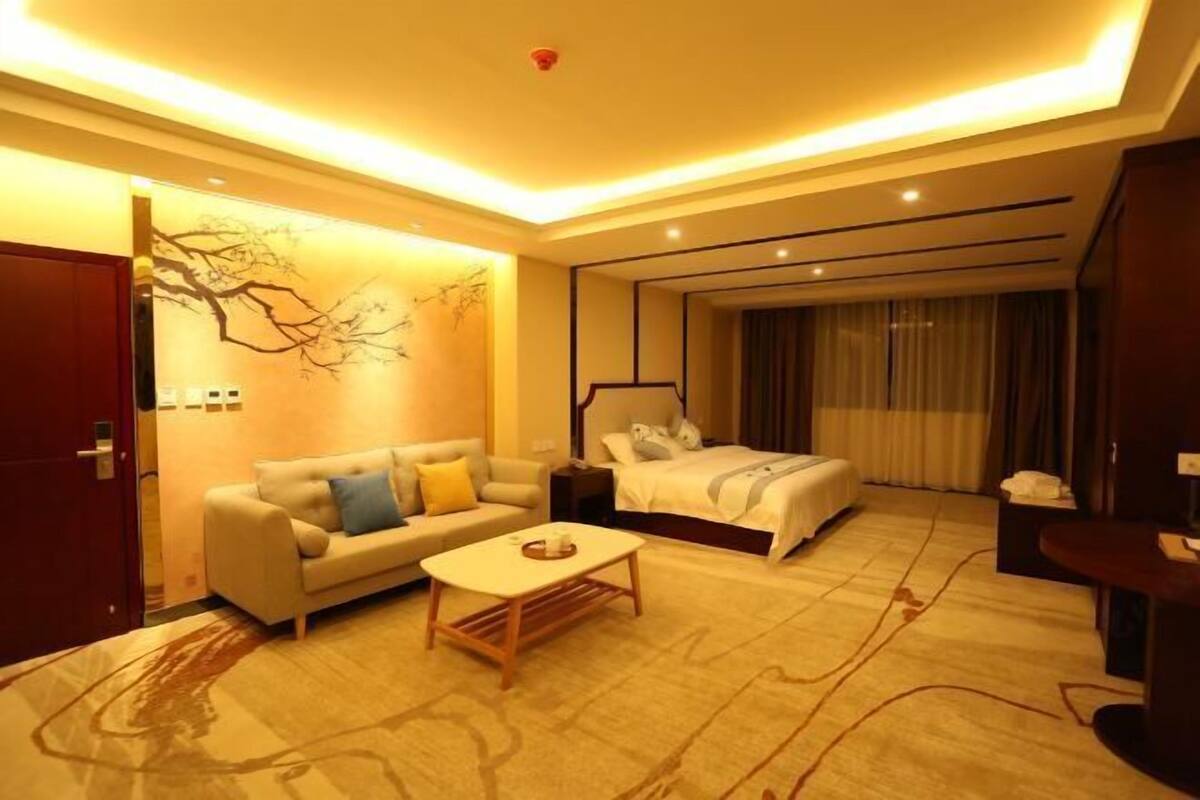 A hotel room with a bed, a sofa, a coffee table, and a desk.