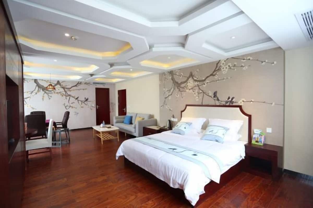 A hotel room with a large bed, a desk, a chair, and a wall with a tree branch mural.