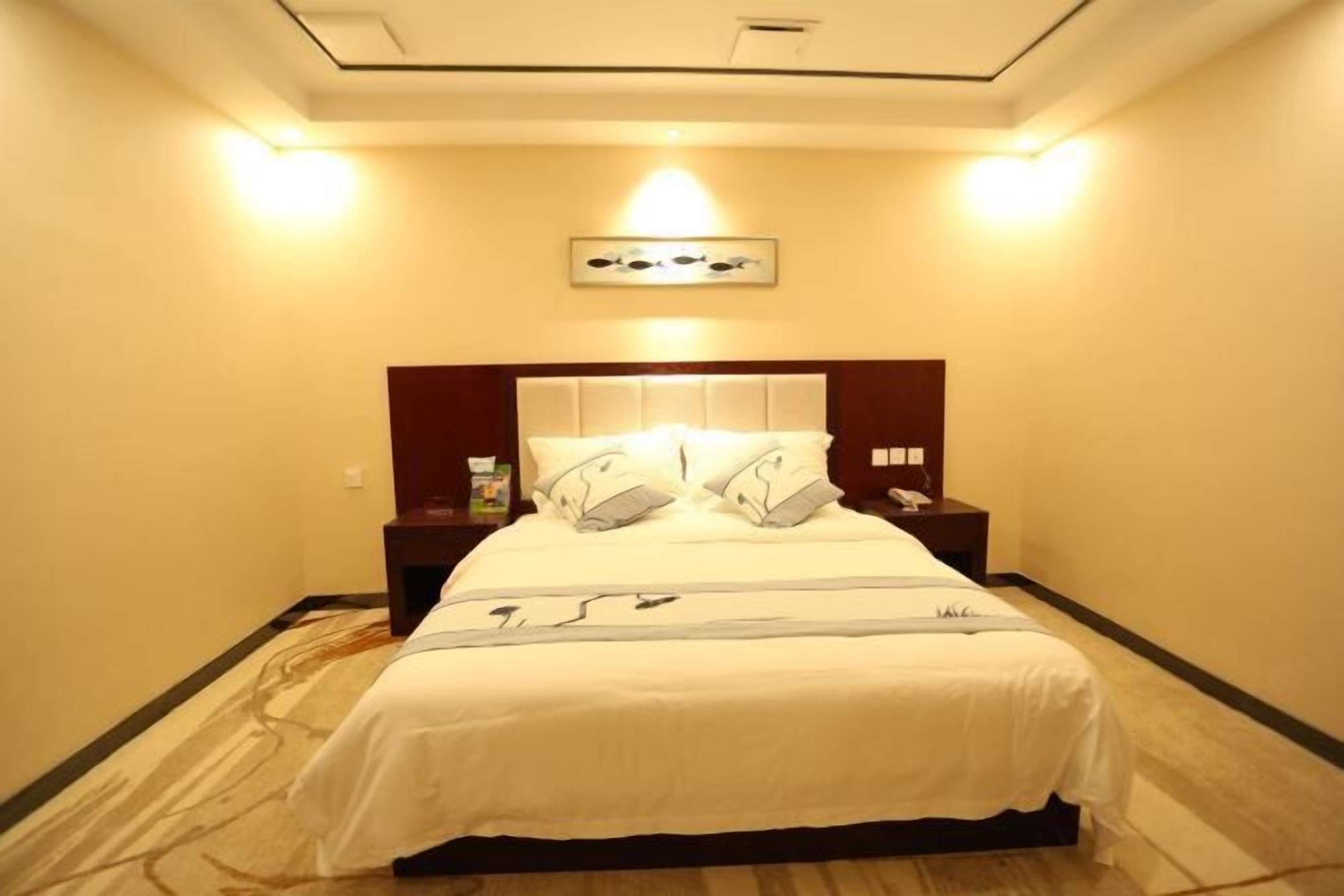 A hotel room with a large bed, a headboard, bedside tables, and a wall-mounted artwork.