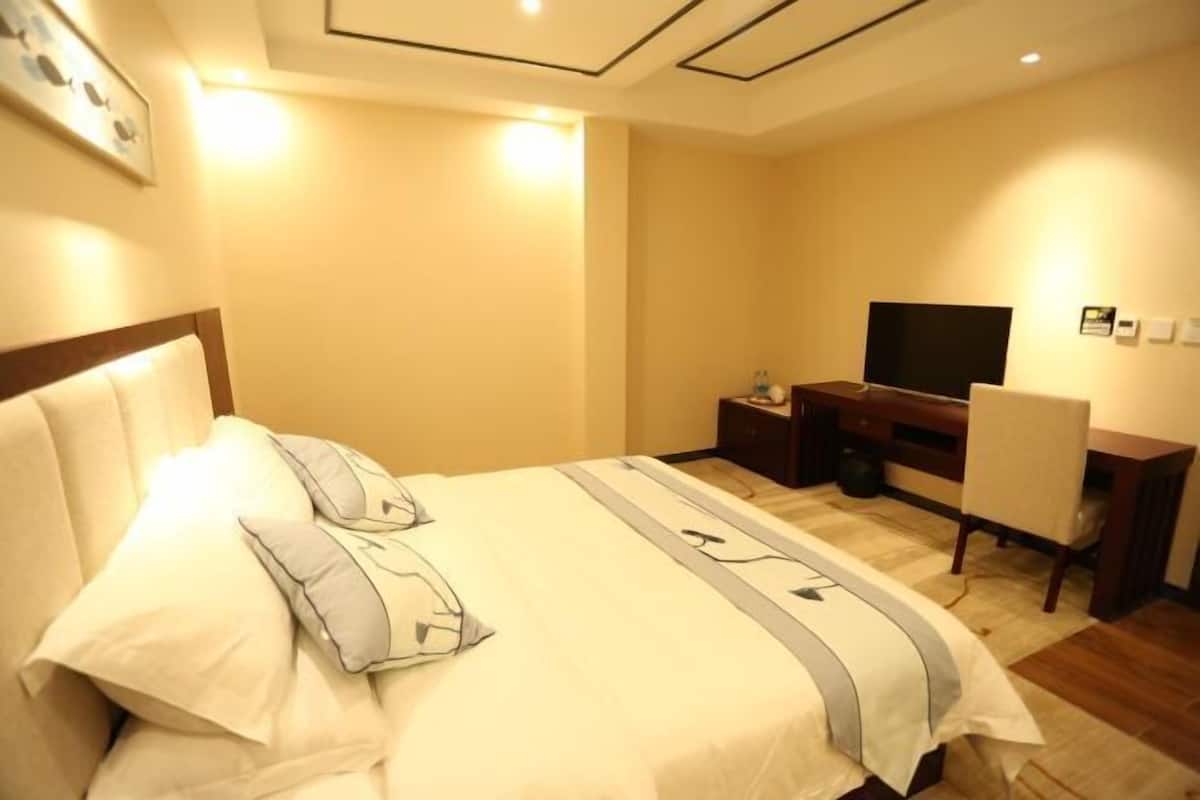 A hotel room with a bed, a desk, a chair, a TV, and a small table.