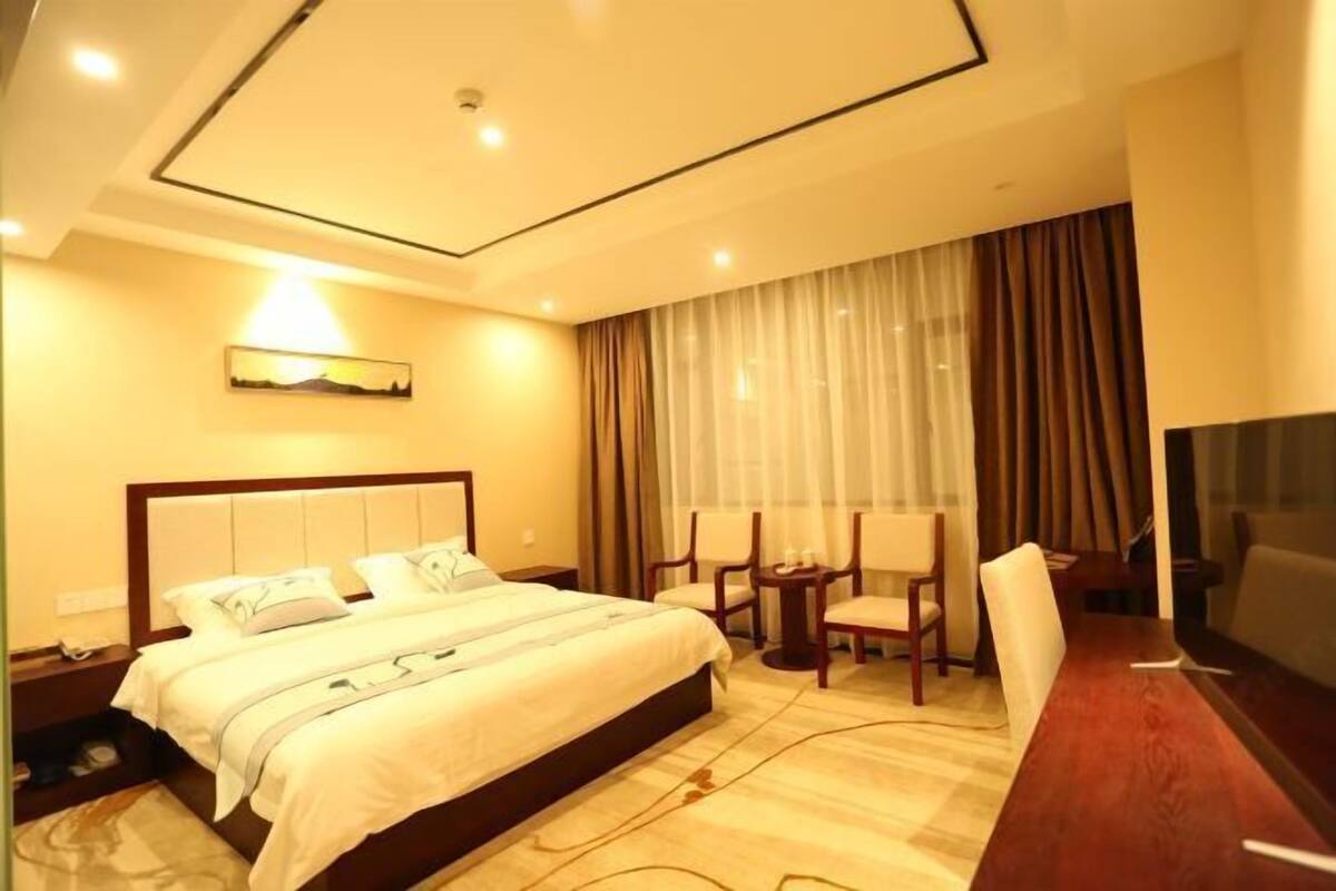 A hotel room with a large bed, a TV, a desk, and a chair.