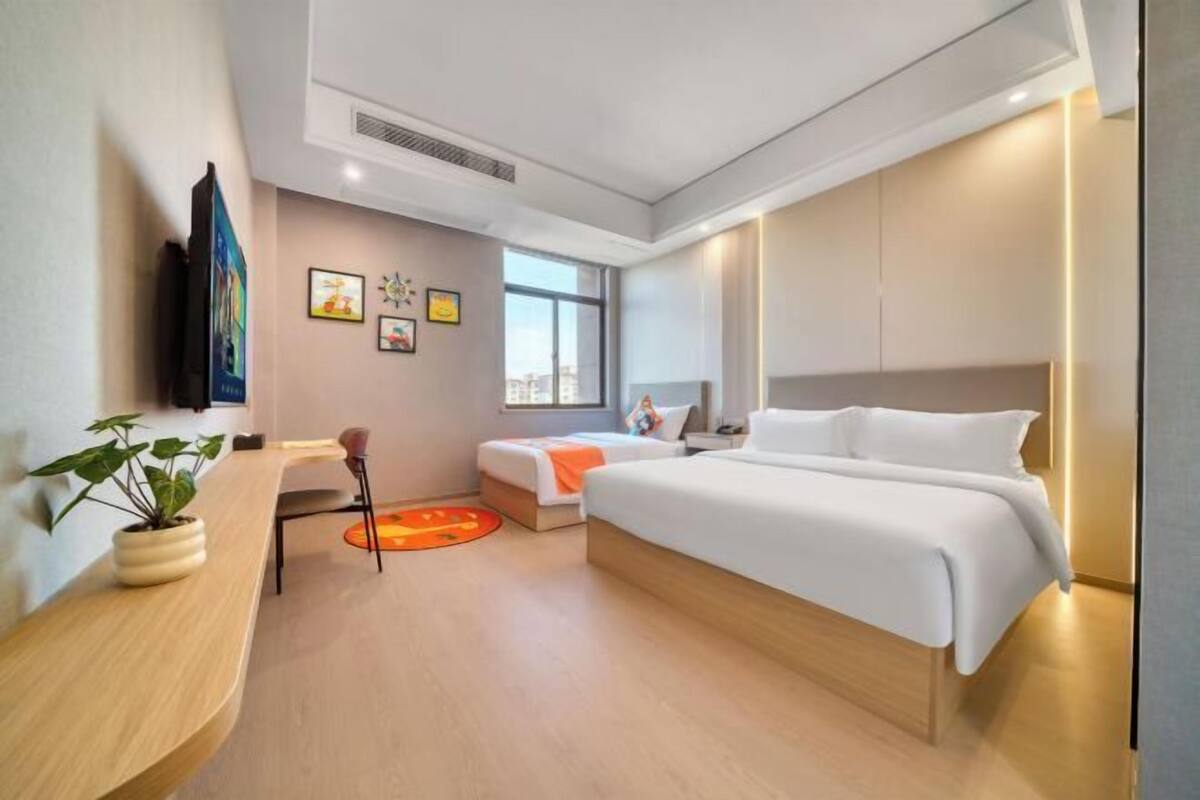 A modern hotel room with a large bed, a desk, a chair, and a potted plant.