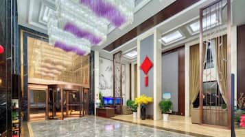 A hotel lobby with a marble floor, a reception desk, and a large chandelier.