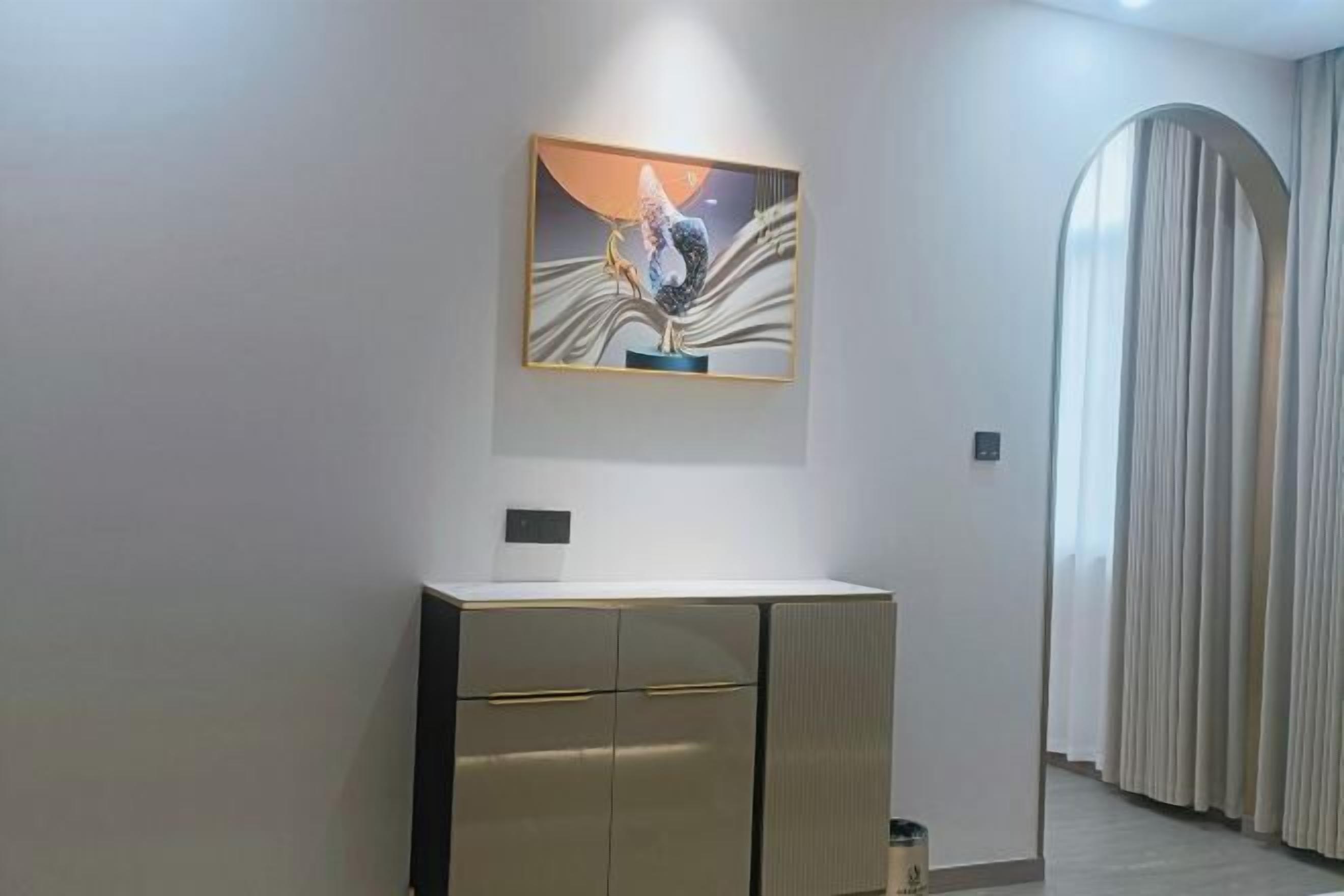 A modern room with a minimalist design, featuring a large artwork on the wall, a sleek cabinet, and a large window with curtains.