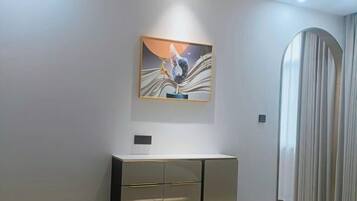 A modern room with a minimalist design, featuring a large artwork on the wall, a sleek cabinet, and a large window with curtains.