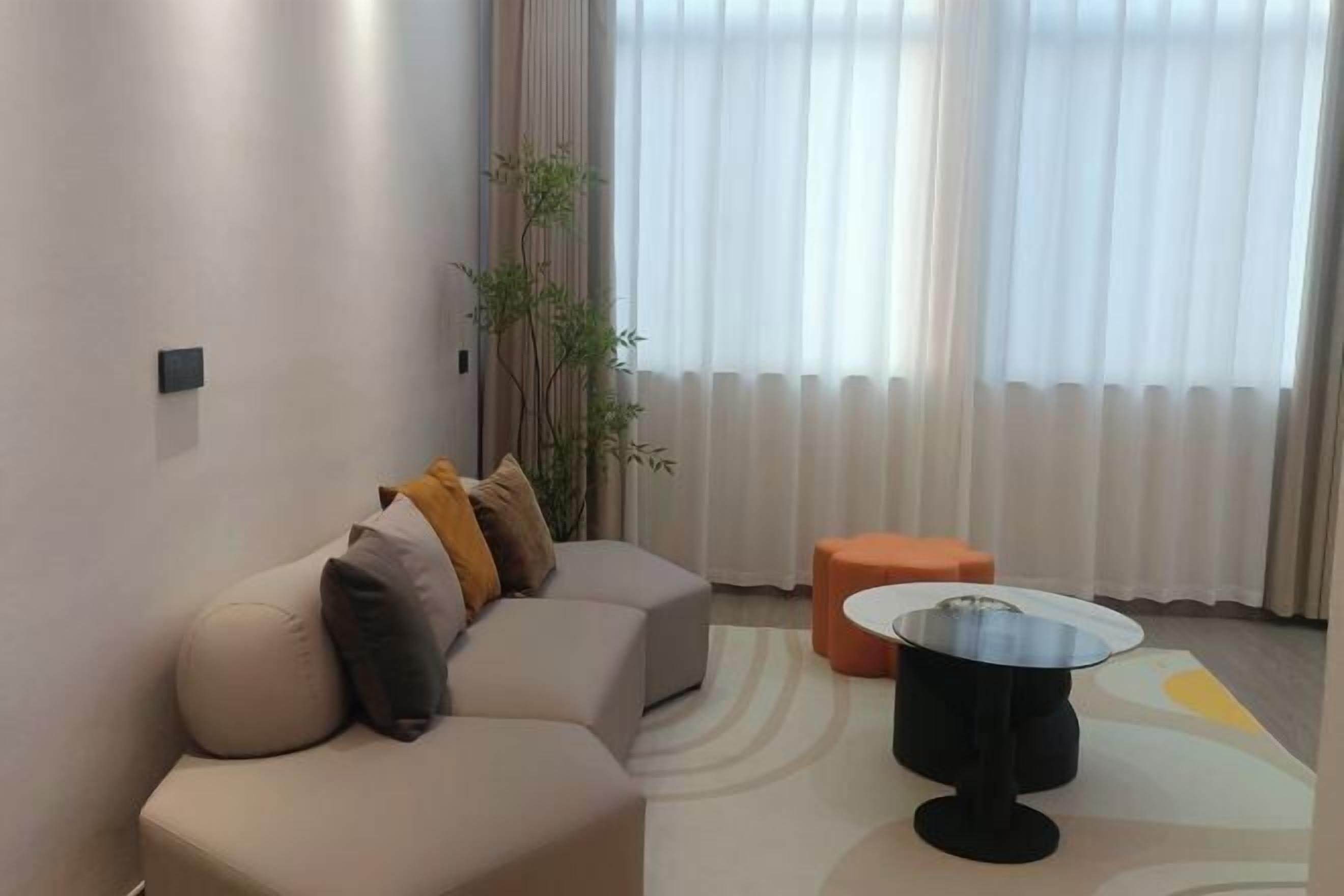 A modern living room with a sectional sofa, a round coffee table, and a small orange ottoman.