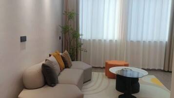 A modern living room with a sectional sofa, a round coffee table, and a small orange ottoman.