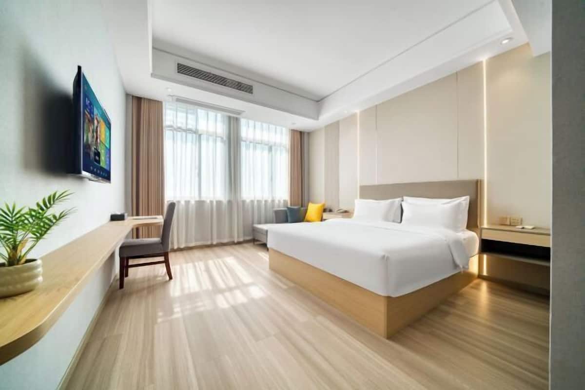 A modern hotel room with a large bed, a desk, a chair, and a TV on the wall.