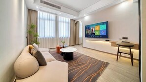 A modern living room with a sofa, a coffee table, a TV, and a small table with a chair. - Waterfront Garden Hotel (Huzhou)
