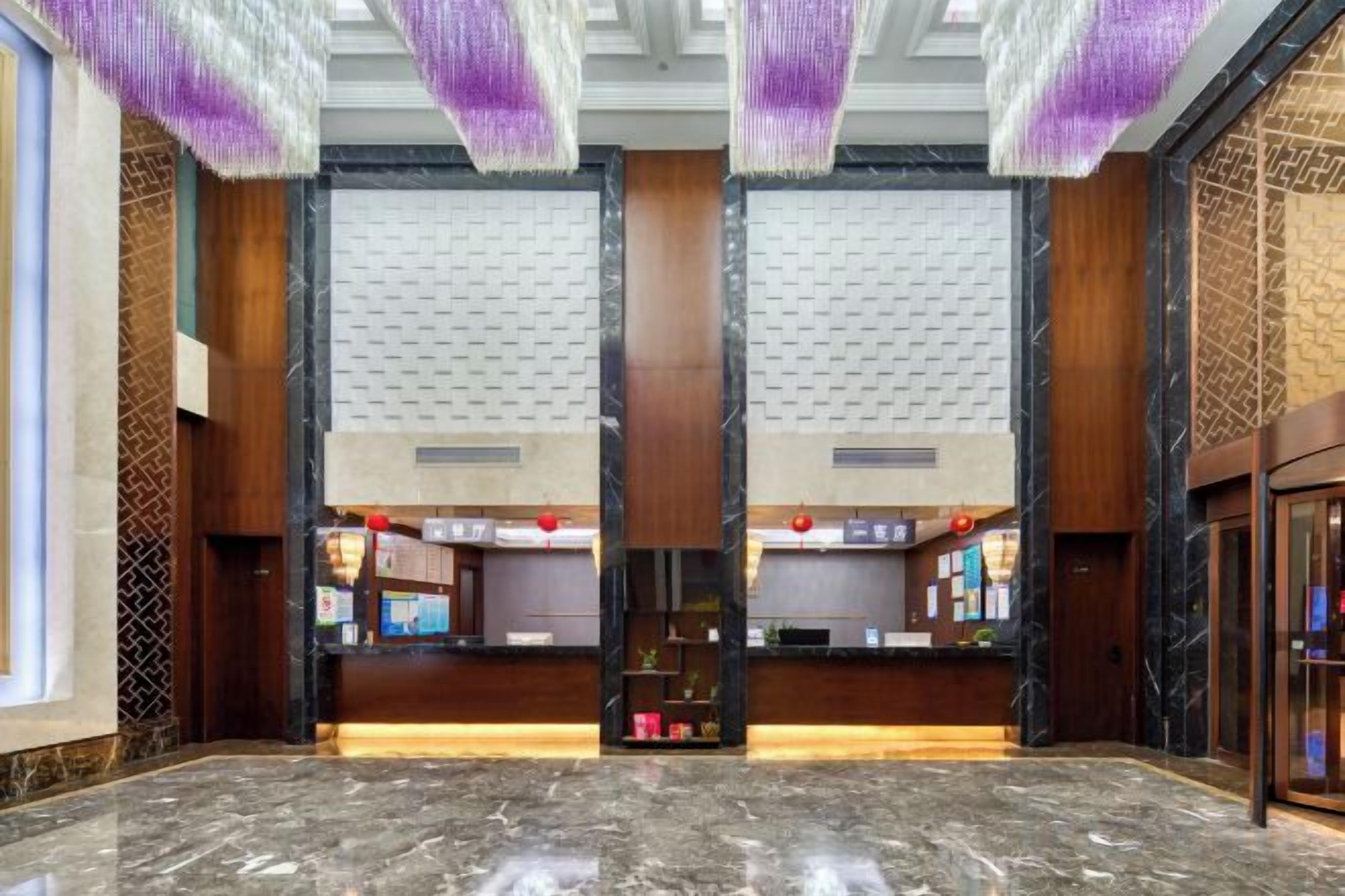 A lobby with a reception desk, marble flooring, and a high ceiling with hanging decorations.