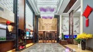 A hotel lobby with a marble floor, a reception desk, a turnstile, and a wall with traditional artwork. - Waterfront Garden Hotel (Huzhou)