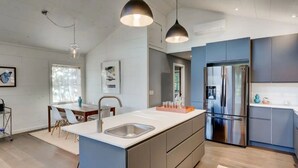 Een moderne keuken met een groot eiland, roestvrijstalen apparatuur en hangende lampen.