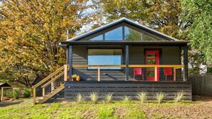 Een moderne cabin met een houten terras, een rode deur en een trap naar de ingang.