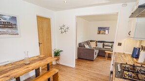 Una cocina moderna con encimera de madera y estufa a gas. Hay una zona de comedor con mesa y bancos de madera. Se ve un sofá gris al fondo.