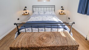 Un dormitorio con cama, lámparas de noche, un cuadro en la pared y un banco de fibras naturales.
