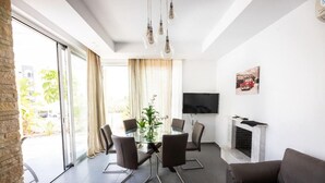 Ein modernes Wohnzimmer mit Glastür zum Balkon, einem Essbereich mit Tisch und Stühlen, einem an der Wand montierten Flachbildfernseher und einem Kamin.