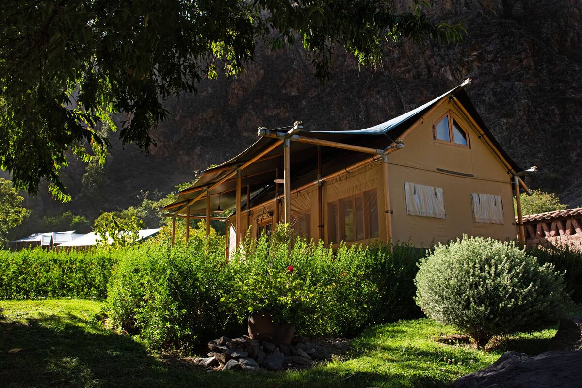 Un chalet doté d’un toit en pente, entouré d’une végétation luxuriante et adossé à un paysage montagneux.