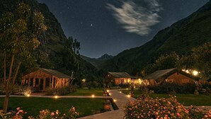 Een sterrenhemel boven een bergachtig landschap met twee verlichte hutten.